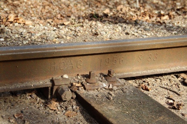 061 Ganz jung ist diese von der HOAG (Hüttenwerke Oberhausen AG) 1956 gewalzte Schiene nicht mehr.<br />Der verdrehte Kopf der rechten Schwellenschraube zeugt eindeutig von zuviel Kraft.<br />Links von der Schwelle ist eine, der in der Steigung verbauten, Wanderschutzklemmen zu sehen.<br />Foto Regine M.